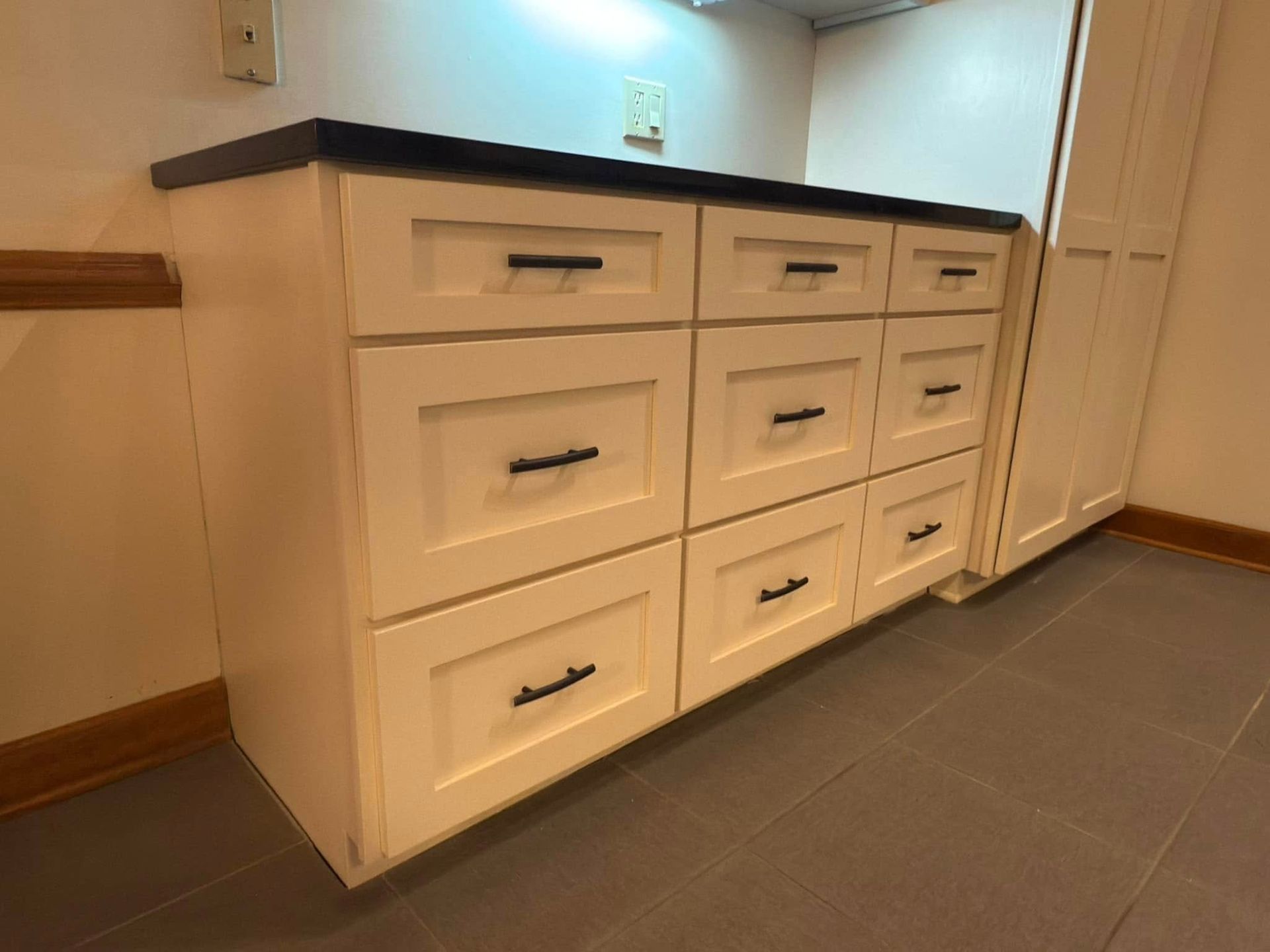 A white cabinet with black handles and drawers in a kitchen.