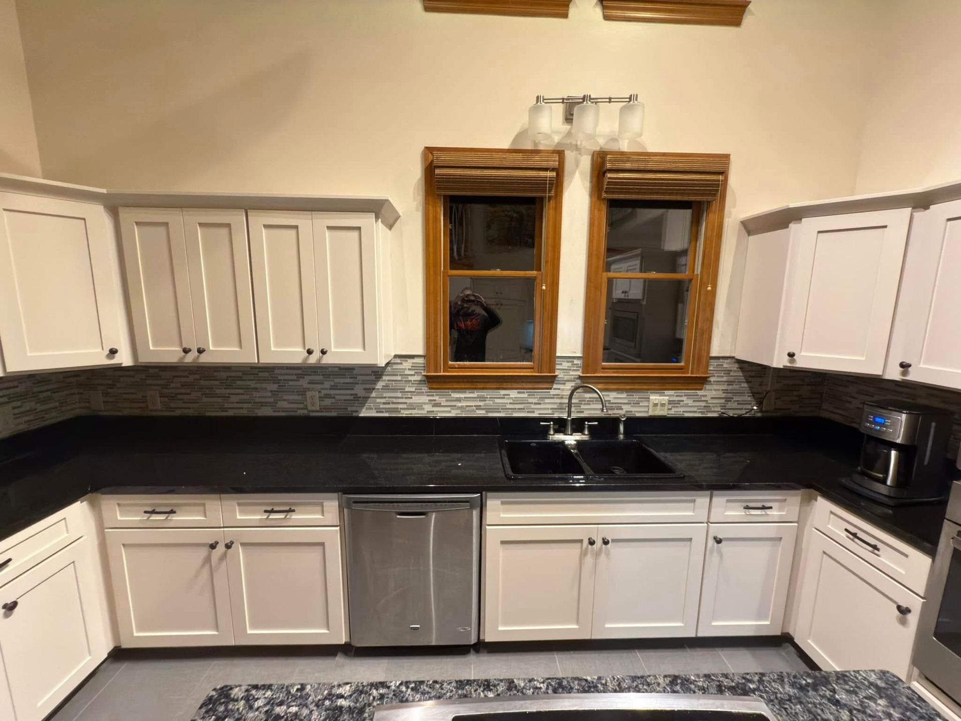 A kitchen with white cabinets , black counter tops , and stainless steel appliances.