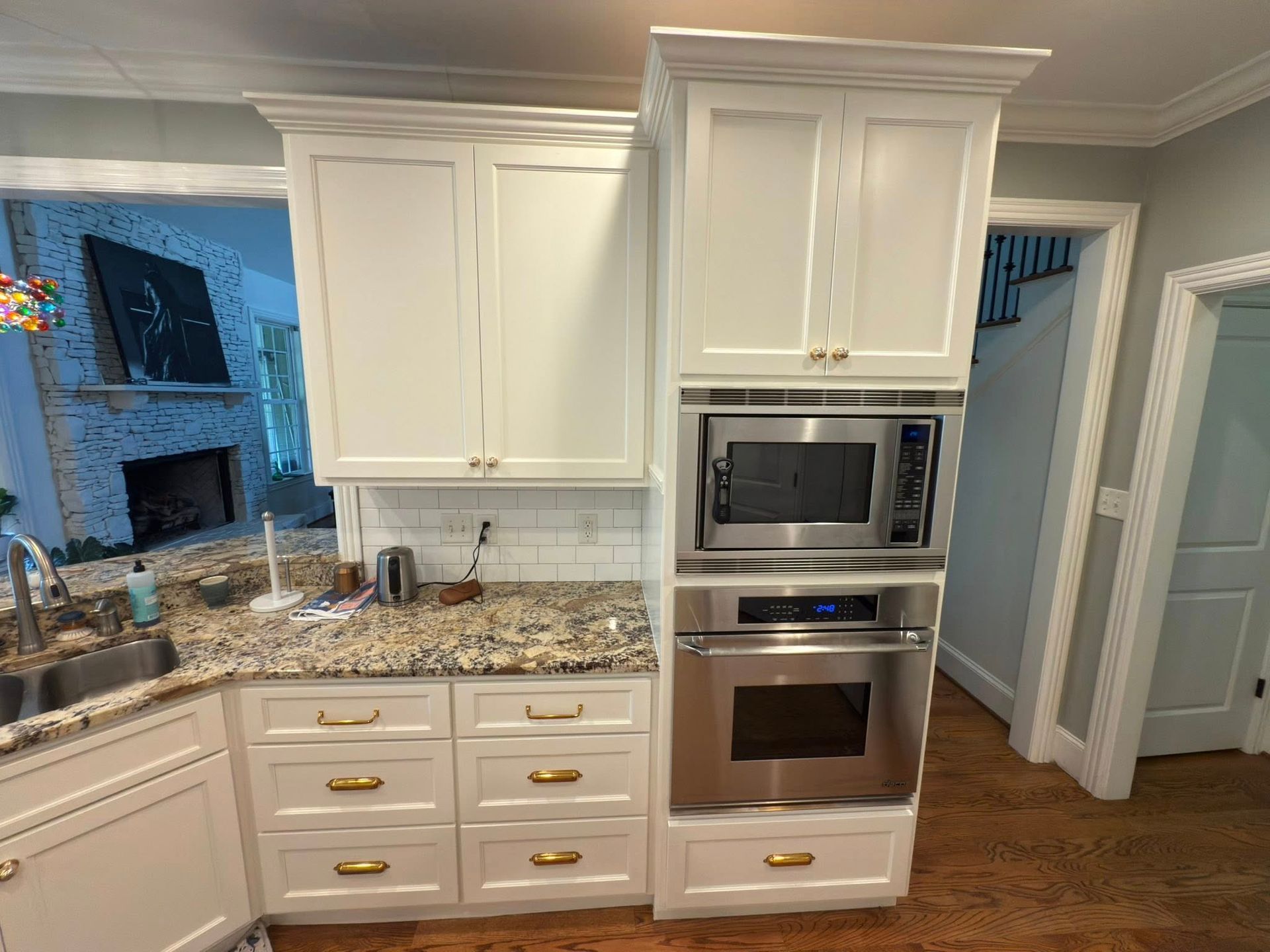 White kitchen cabinets with built-in microwave and oven, granite countertop, gold hardware.