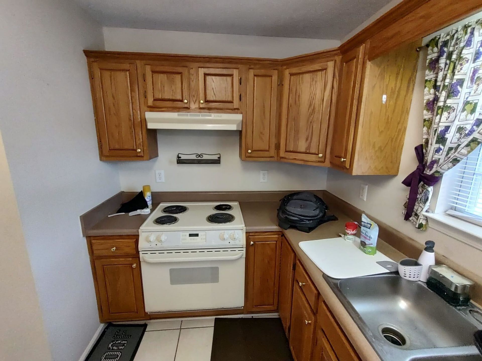 A kitchen with wooden cabinets , a stove , a sink and a window.