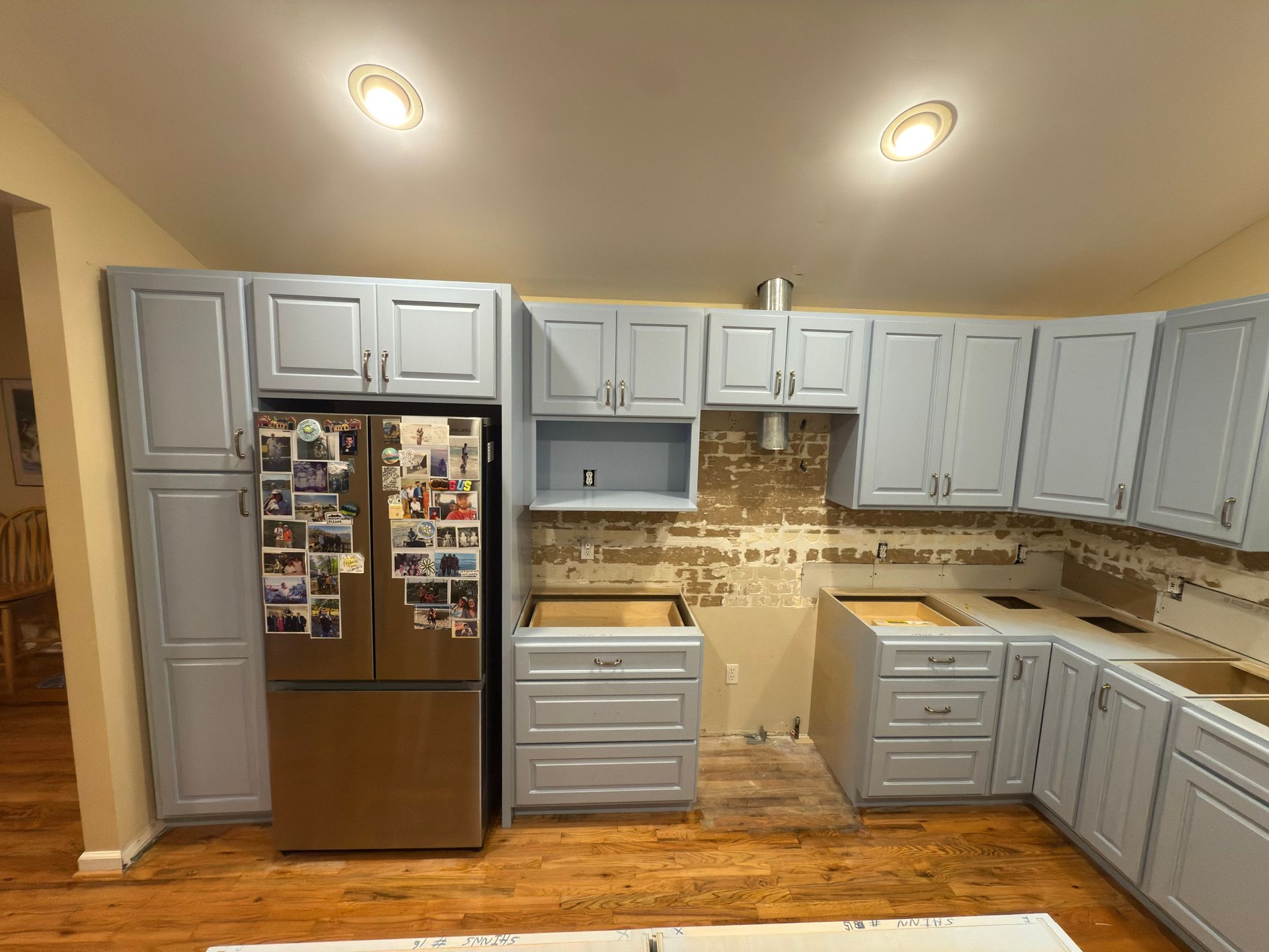 Kitchen renovation with blue cabinets, stainless steel refrigerator, and exposed wall.