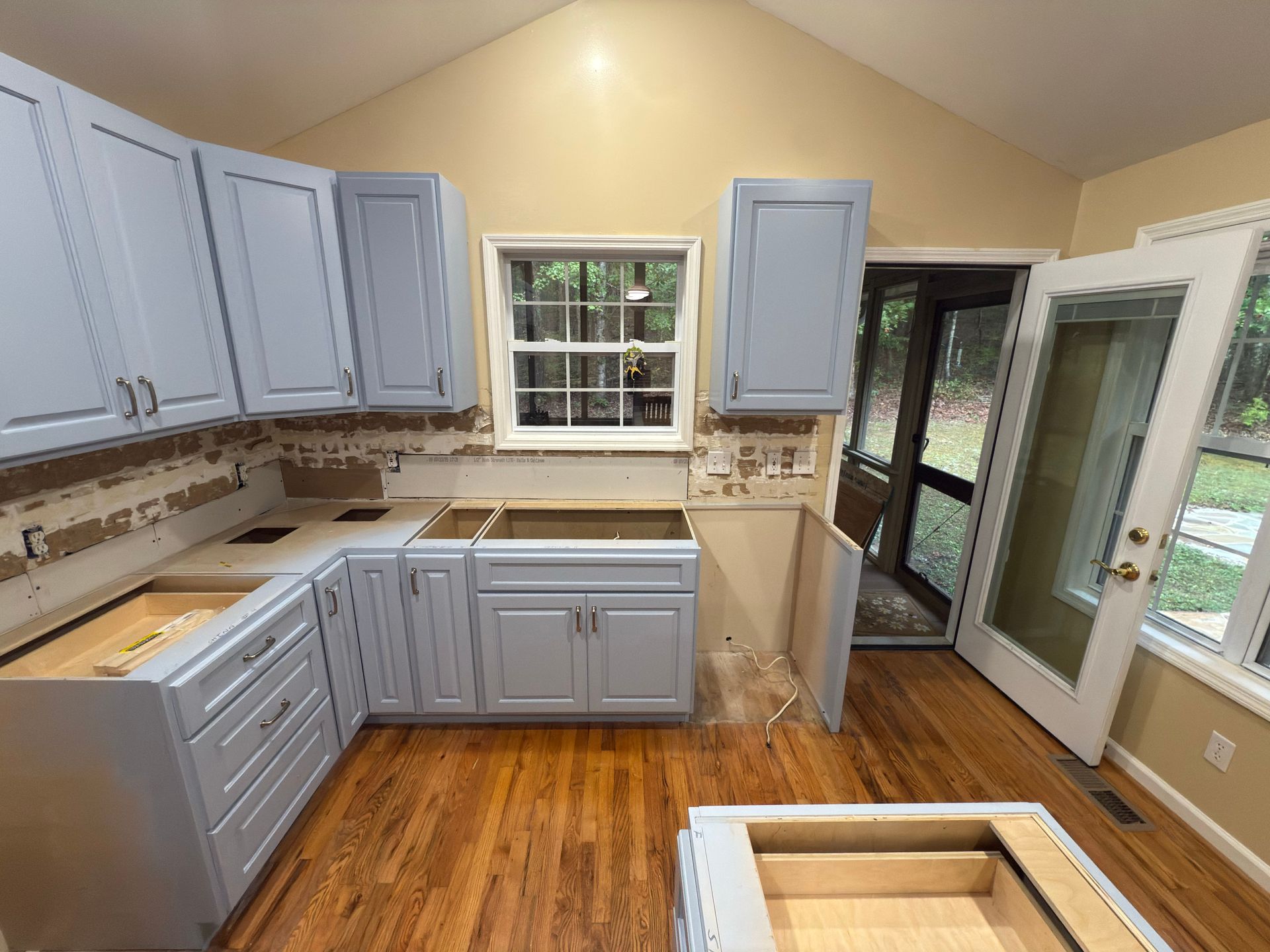 Kitchen cabinets being installed, light blue with exposed drywall. Hardwood floors and French doors.