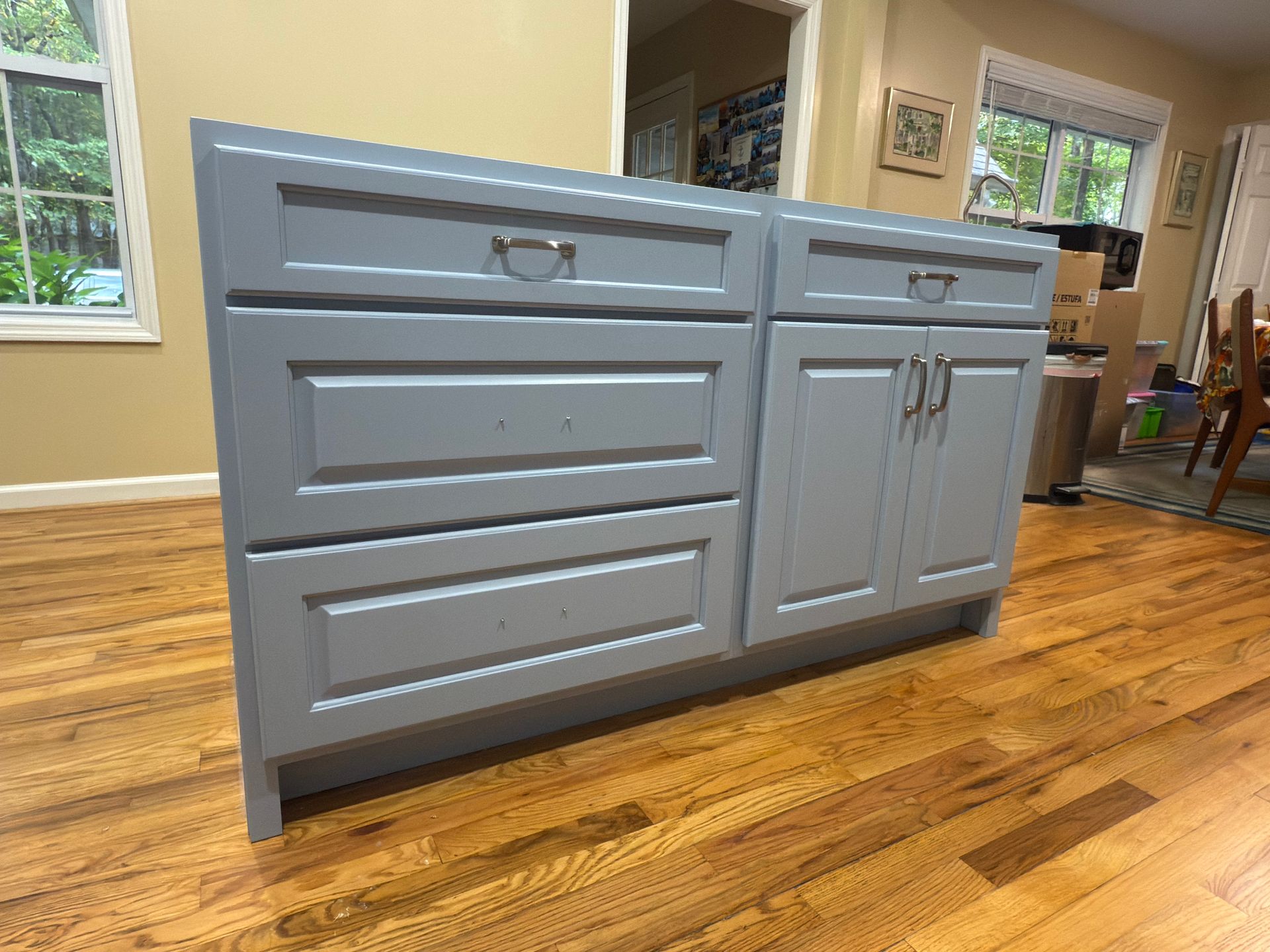 Gray kitchen cabinet with drawers and doors on a hardwood floor.
