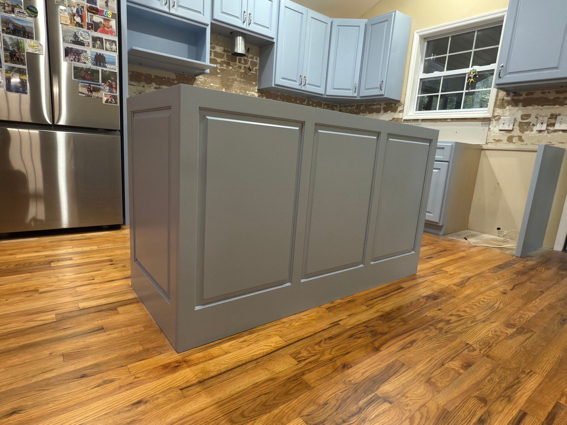 Gray kitchen island with decorative panels on a hardwood floor, with blue cabinets in the background.