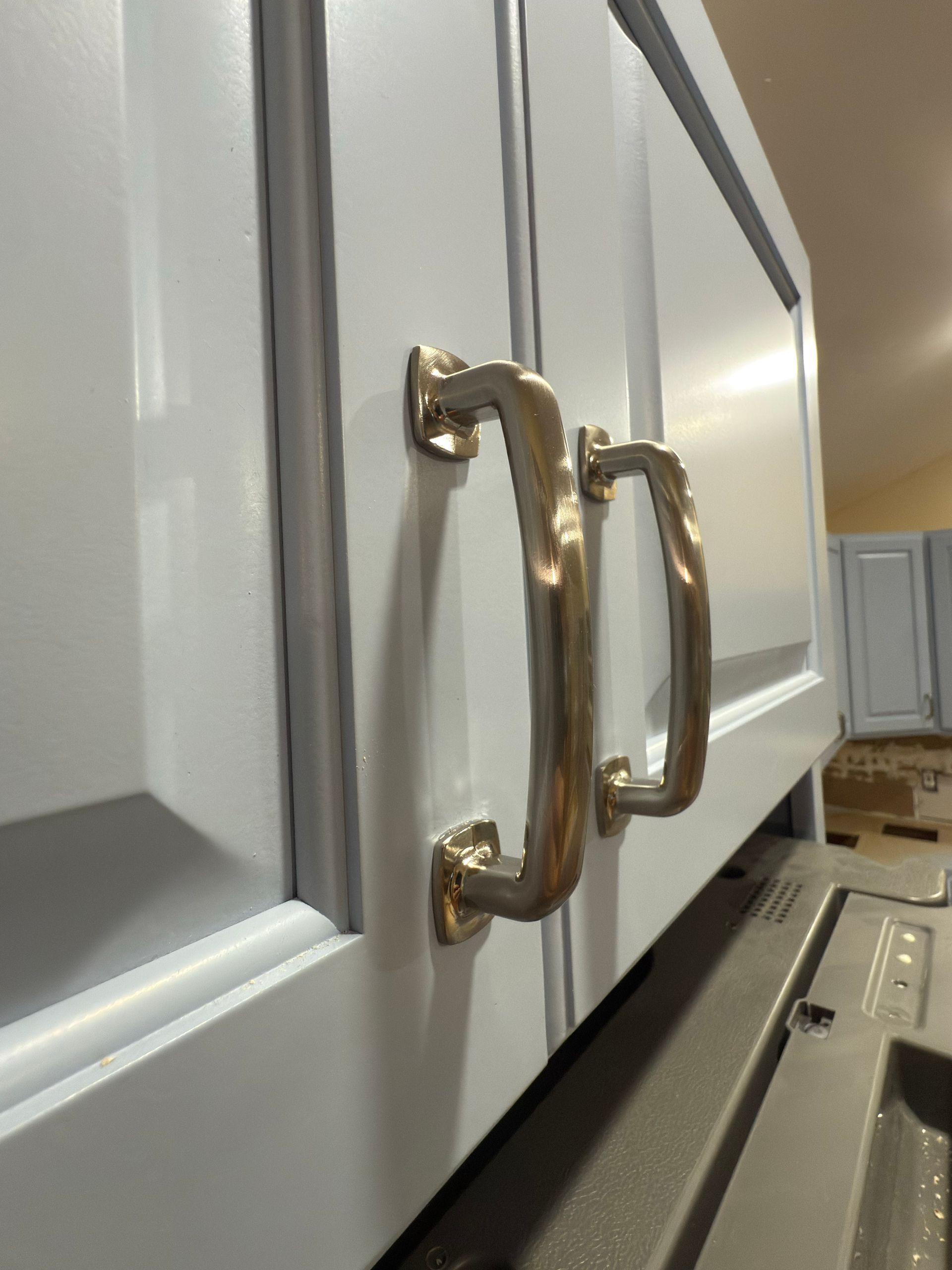 Close-up of two cabinet handles with a gold finish on a gray cabinet door.
