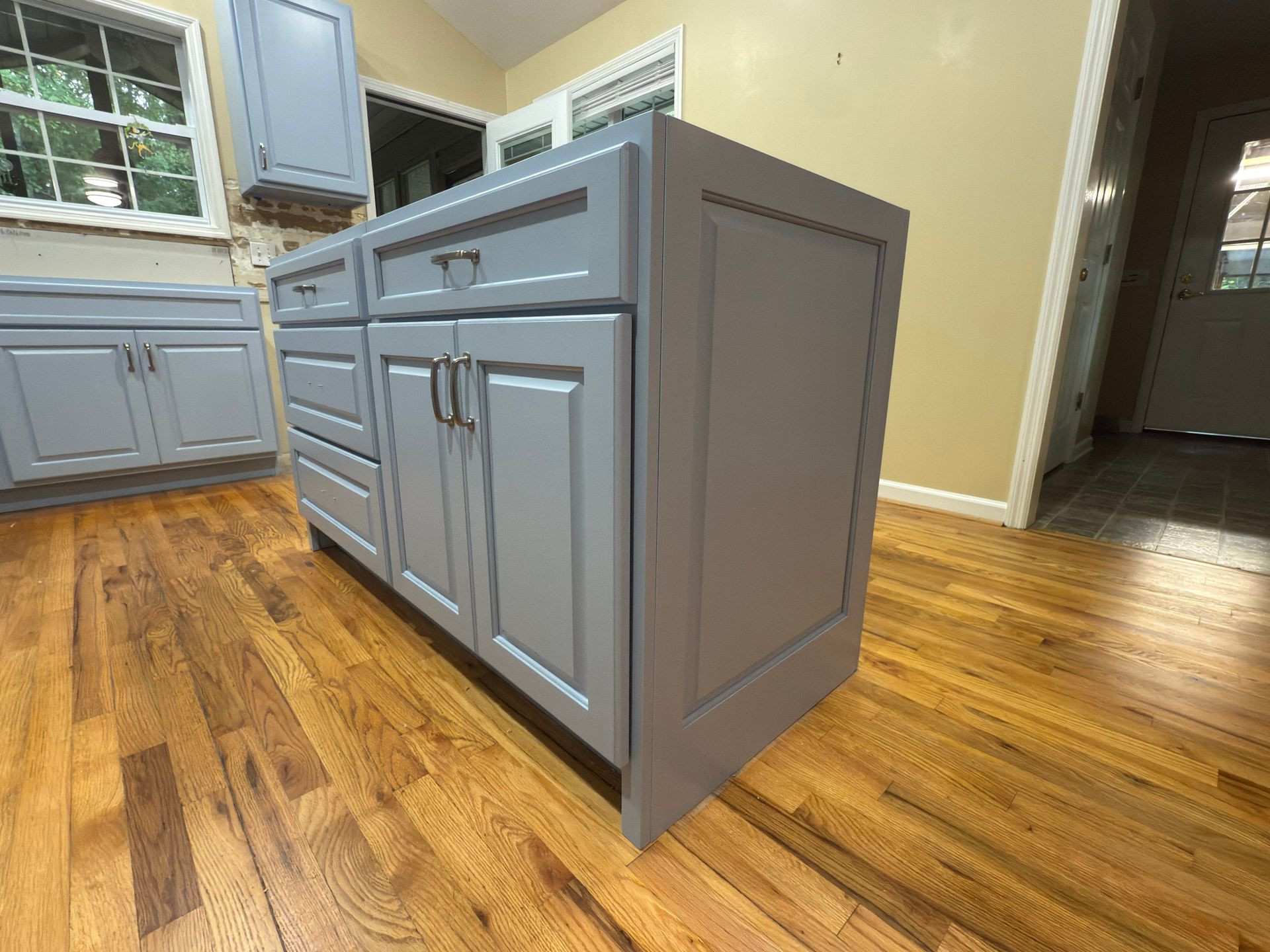 Gray kitchen island with cabinets and drawers, set on hardwood floor.