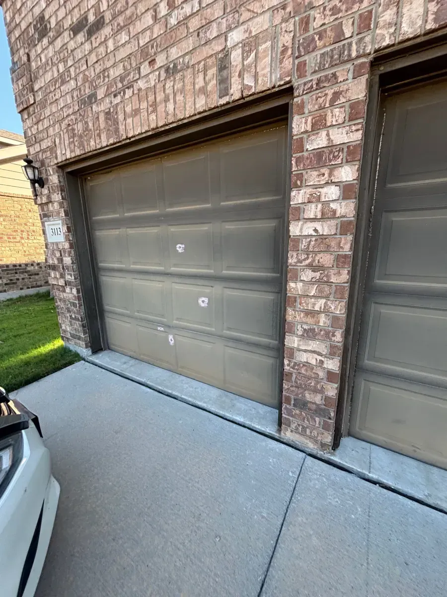 A partial view of two brown garage doors set into a brick exterior wall next to a concrete driveway.