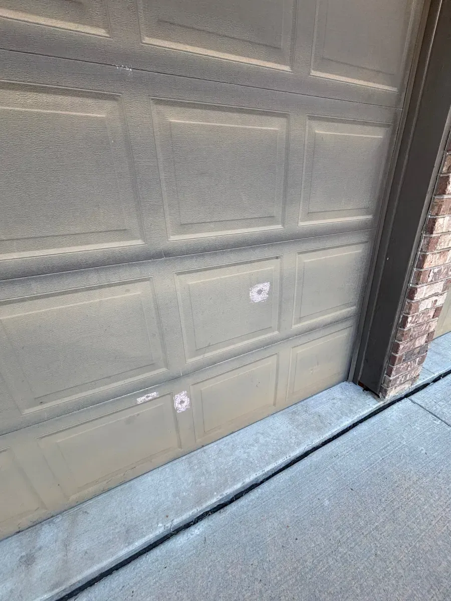 Tan-colored garage door sections featuring small, white circular stickers or damage marks on two of the panels.