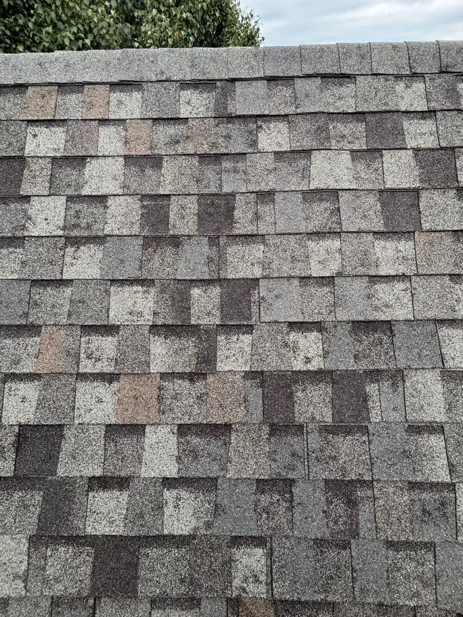 A close-up of a weathered, grey-toned asphalt shingle roof with a repetitive, multi-hued rectangular pattern.