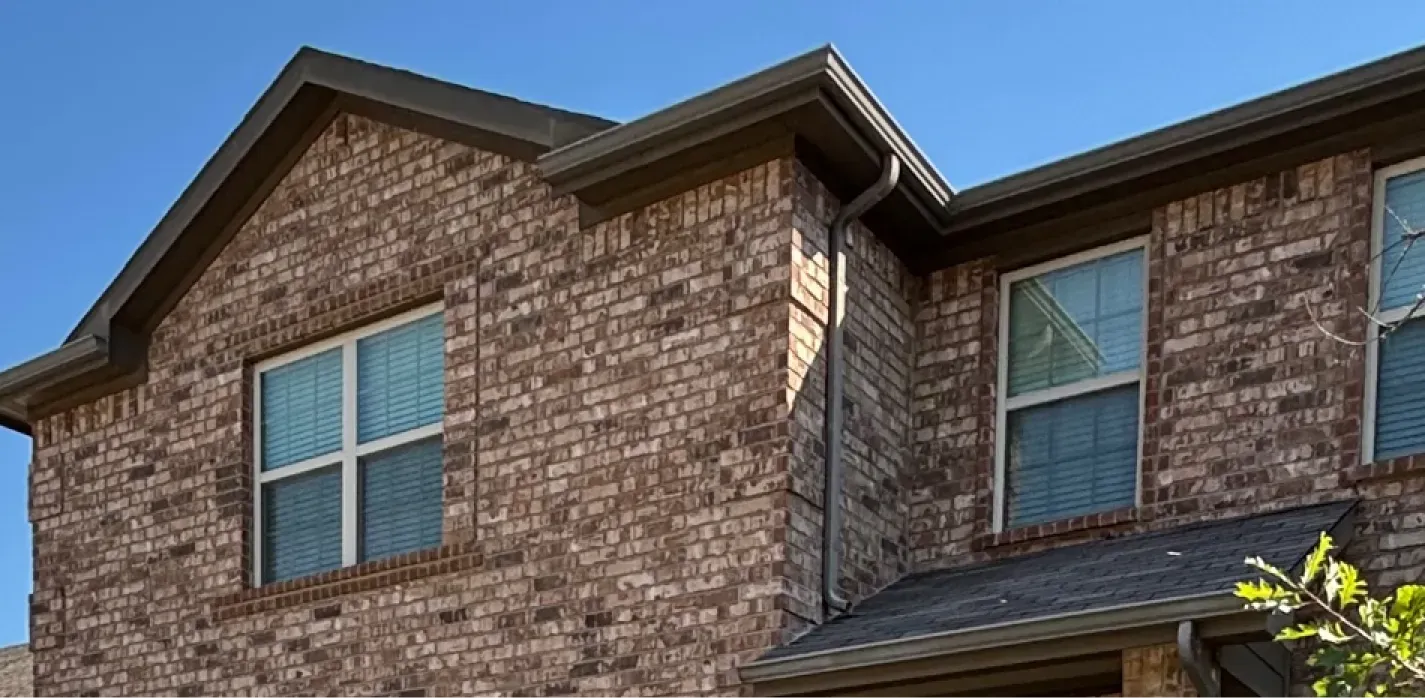 A close-up view of the exterior brick wall and roofline of a multi-story home under a clear blue sky.