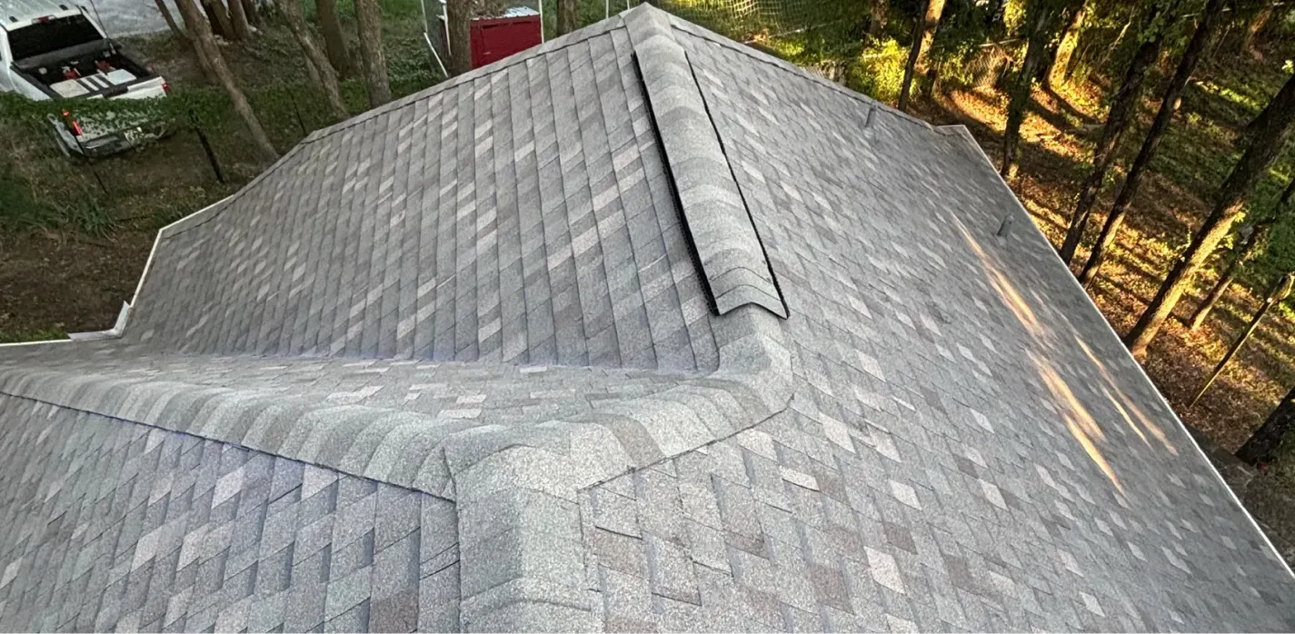 A high-angle view of a grey shingled residential roof surrounded by trees.