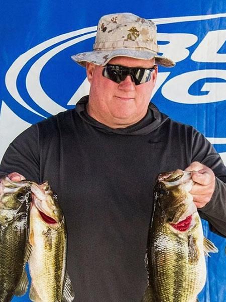 Man in hat and sunglasses holds three large bass. Blue Bud Light backdrop.