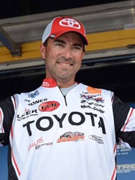 Man in a Toyota hat and shirt smiles, arms slightly raised, likely at a fishing competition.