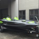 Gray and neon green motorboat on a trailer parked in front of a building.