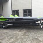 Black and green boat on a trailer, parked in front of a building.