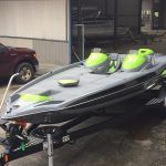 Gray and black boat on a trailer with lime green seats and accents in front of a building.