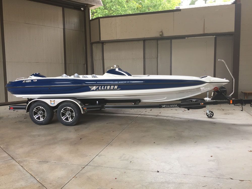 Blue and white Allison XB-2003 boat on a trailer, parked inside a building.