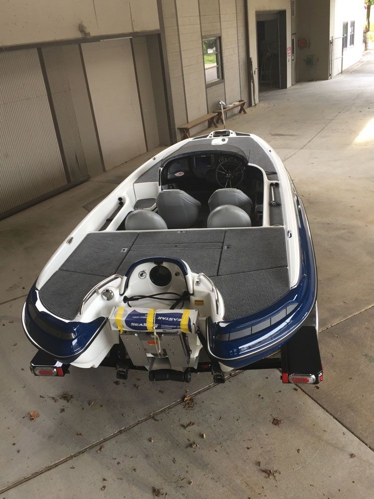 Blue and white bass boat on trailer under a covered area, with dark gray seats and deck.