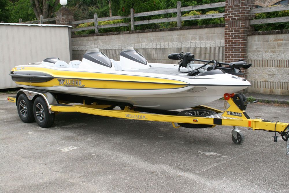Yellow and white boat on a yellow trailer, with a white jet ski. Parked on asphalt.