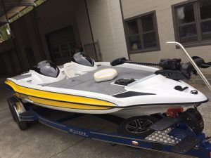 White and yellow motorboat on a blue trailer, parked in front of a building with windows.