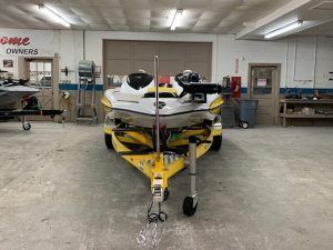 Yellow and white boat on a trailer inside a workshop.
