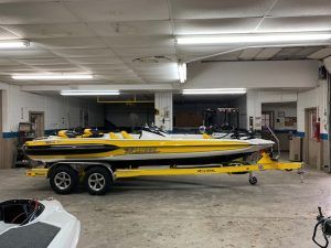 Yellow and white speedboat on a trailer inside a garage, under fluorescent lights.