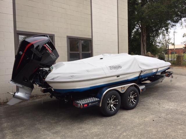 Boat on a trailer, covered with a white tarp, and a large black outboard motor. Gray building in the background.