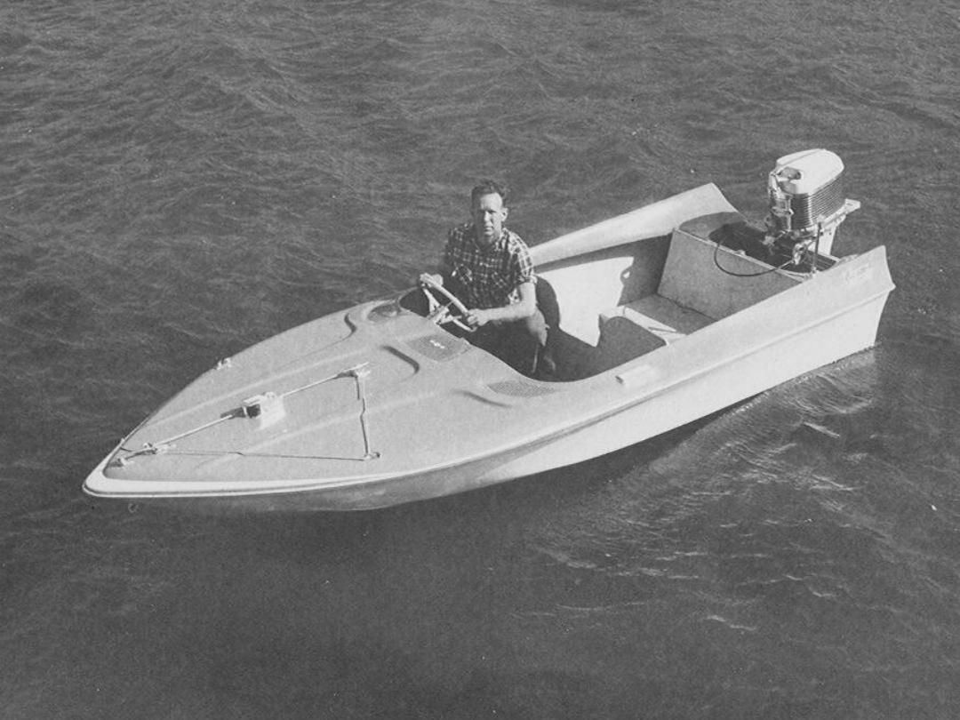 Man sits in small boat on water, operating an outboard motor.