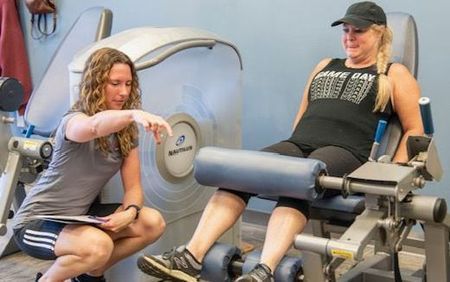 A Woman is Kneeling Down Next to a Woman sitting on a Leg Extension Machine | Uniontown, OH | My Personal Trainer