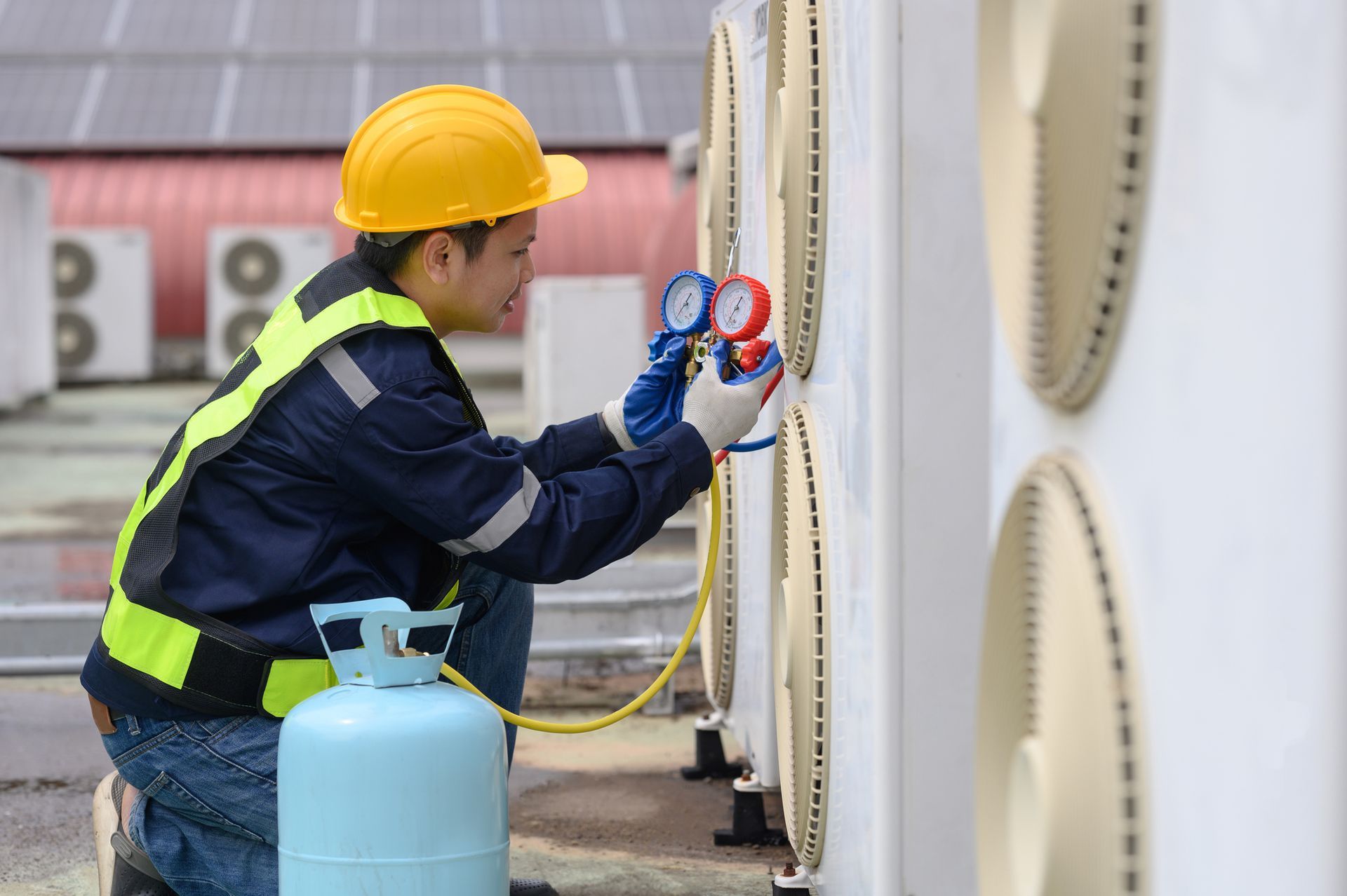 HVAC technician using manifold gauge to check refrigerant on outdoor air conditioning unit.