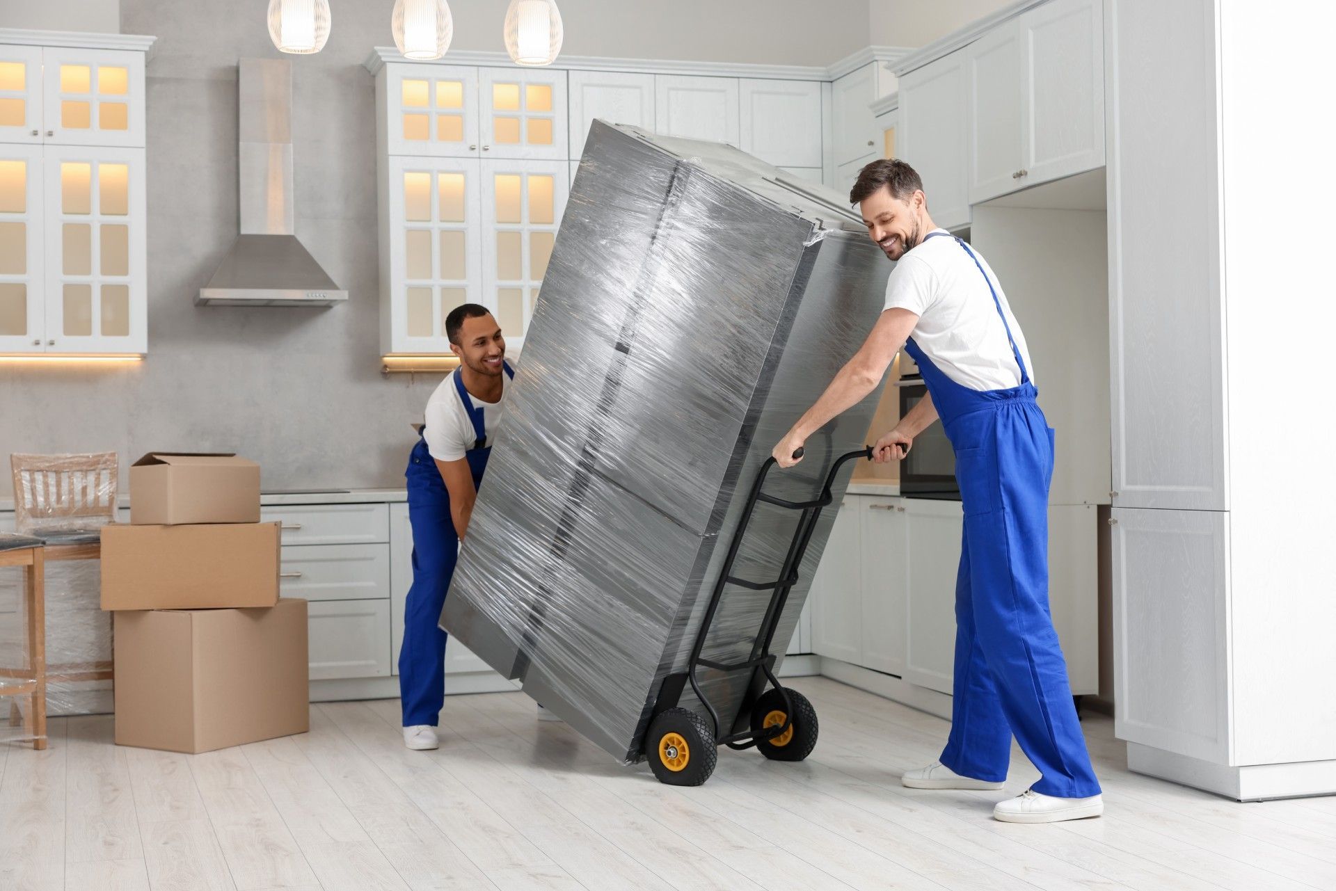 A man is pushing a refrigerator on a dolly in a kitchen.