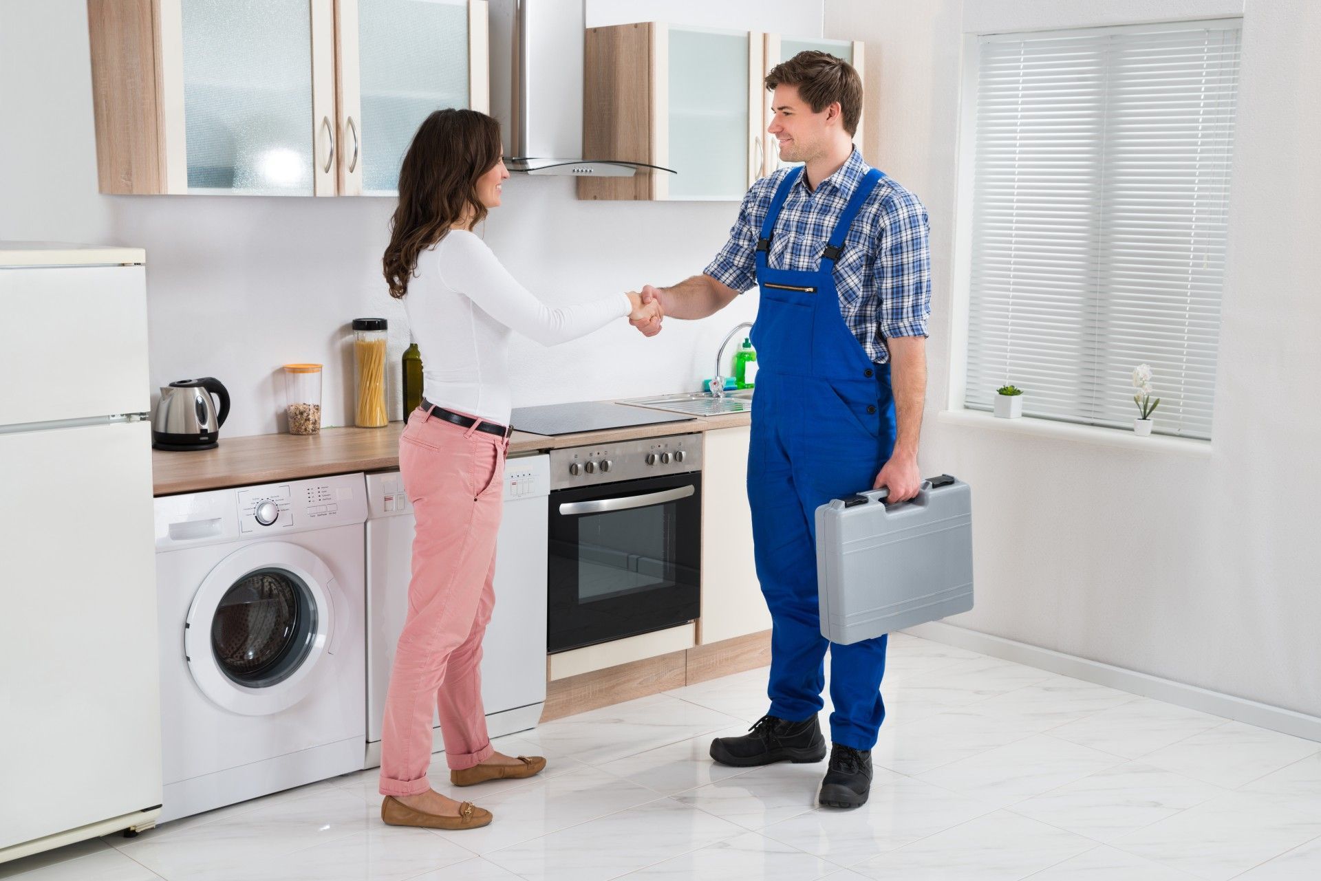 A man in overalls is shaking hands with a woman in a kitchen.