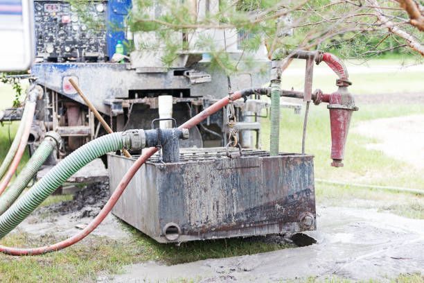 Septic tank pumping truck with hoses and equipment for waste removal on grassy site.