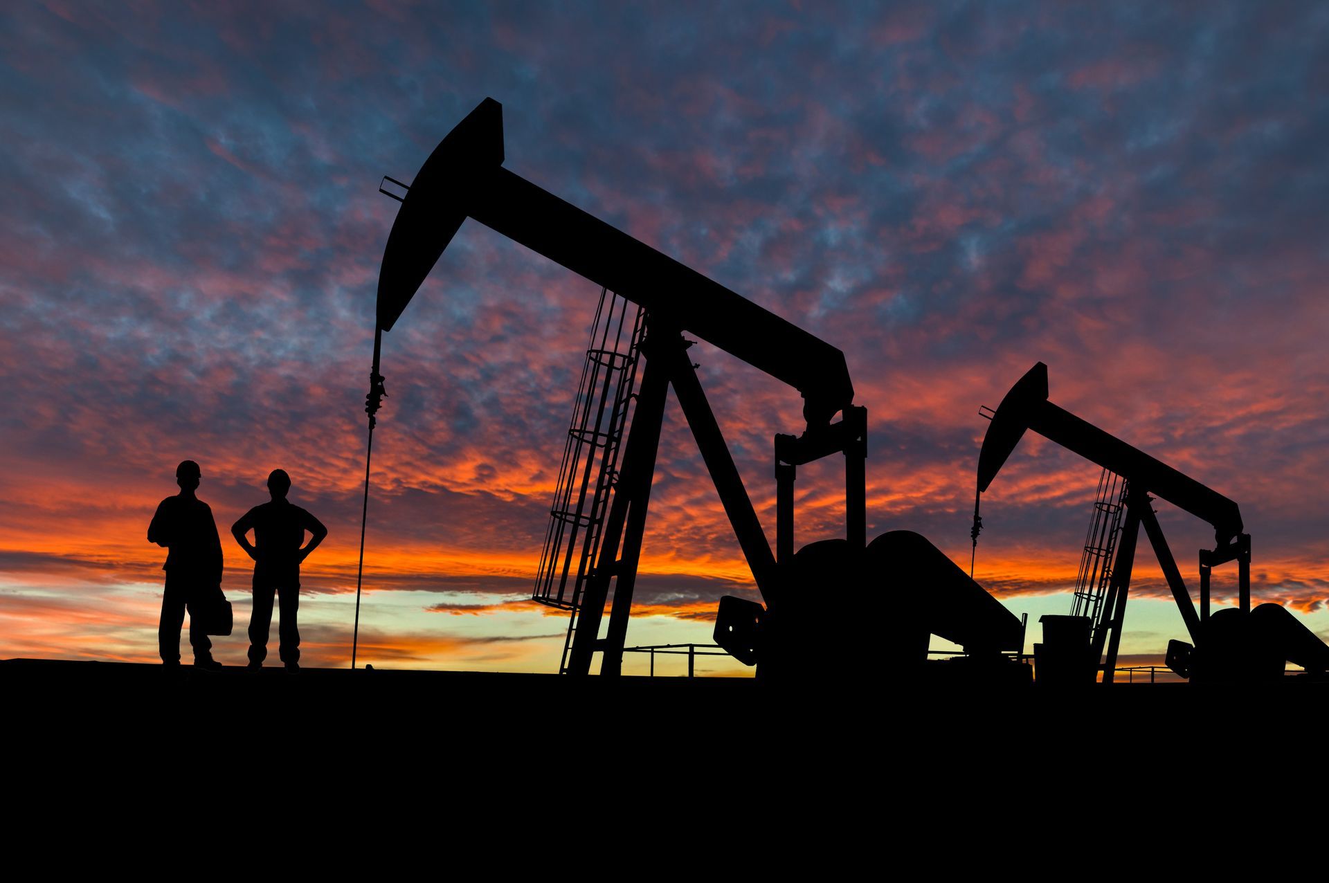 Silhouette of a person standing next to a few oil rigs | Well Pump Service