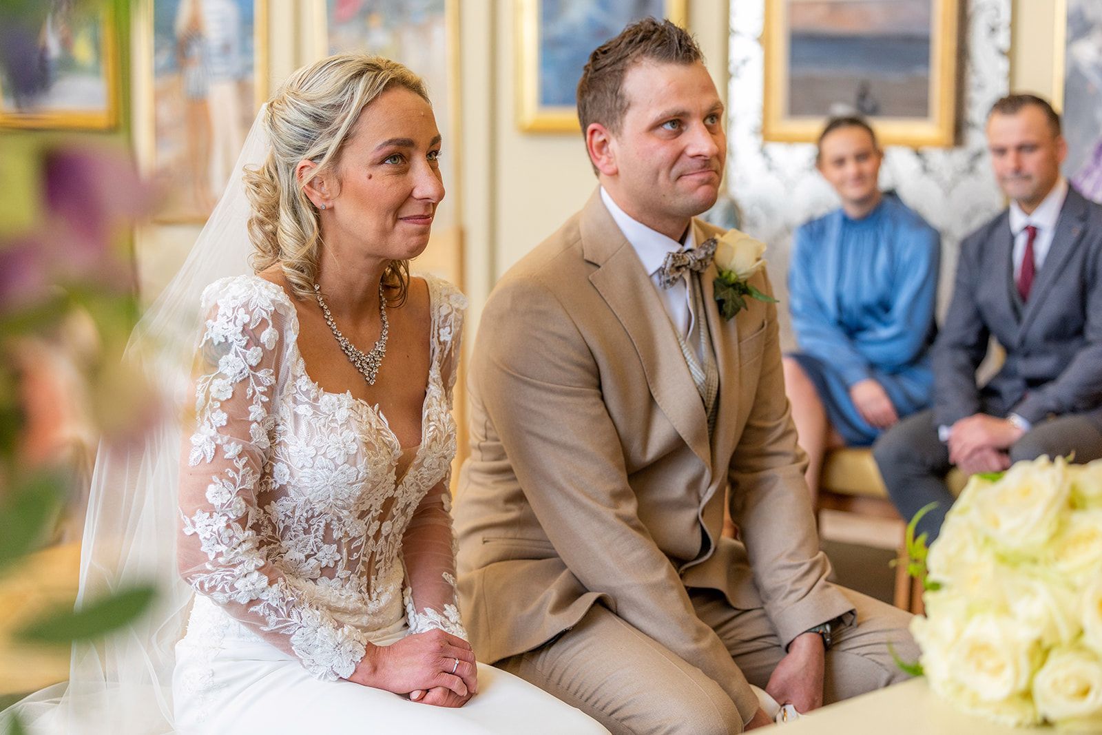 Bruid en bruidegom tijdens een huwelijksceremonie. Zij draagt ​​een witte jurk; hij draagt ​​een beige pak.