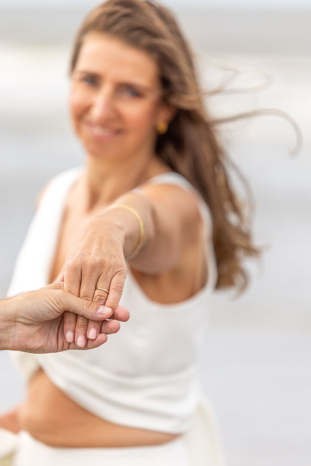 De handen van het echtpaar gevouwen, de trouwringen zichtbaar. Eén hand heeft rode nagellak, de andere draagt ​​een blauw pak.