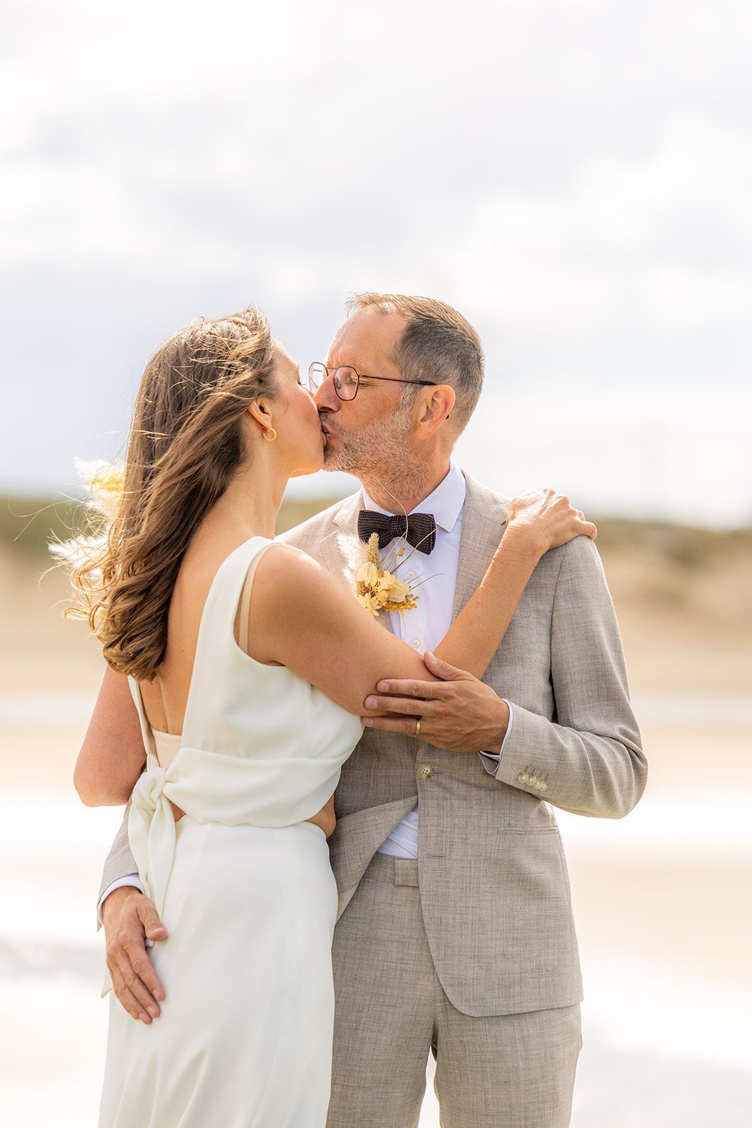 Een stel loopt hand in hand, glimlachend, over een pad; de bruid in een witte jurk, de bruidegom in een roestbruin pak.