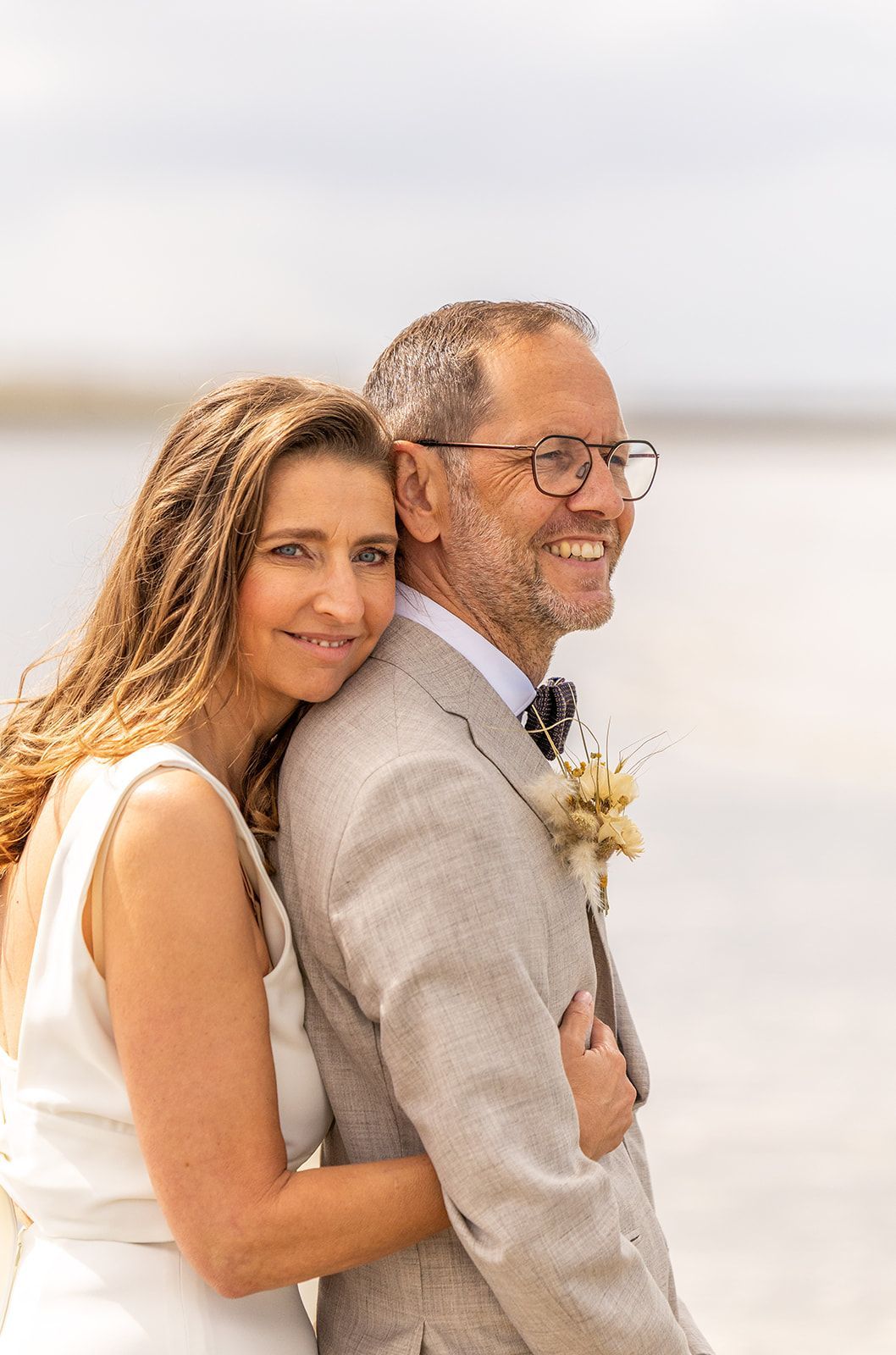 Bruid in kanten topje lacht en houdt de hand van de bruidegom vast. Oceaan op de achtergrond. Zonnige dag.