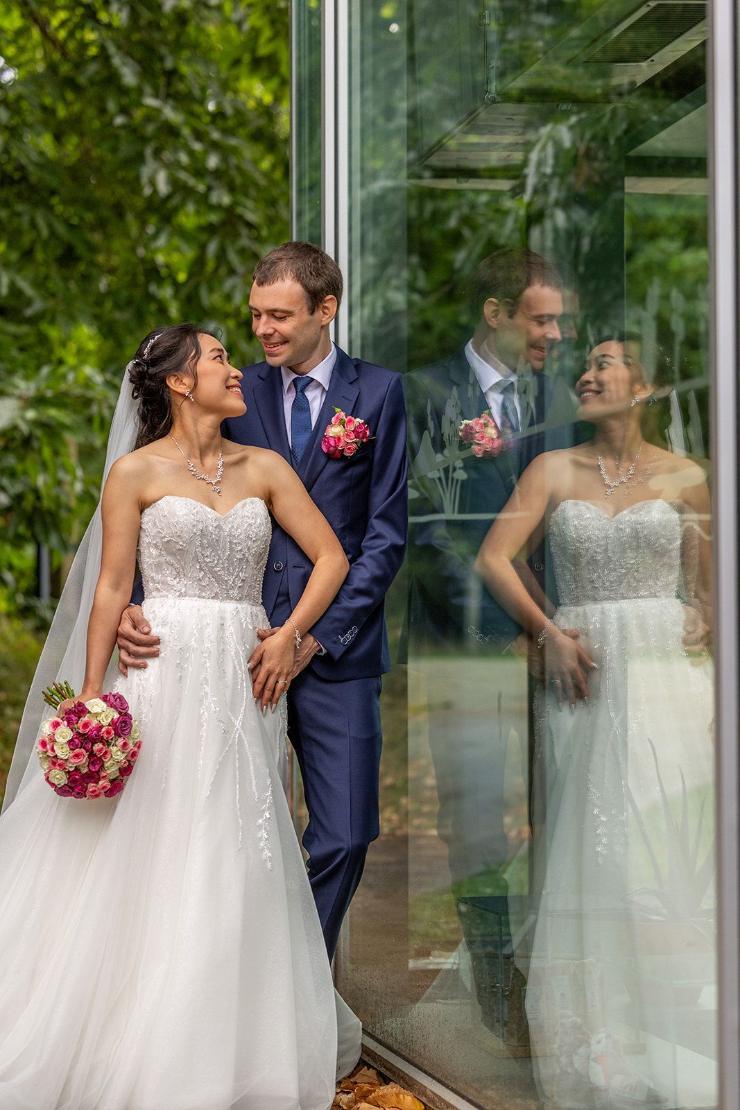 De handen van het echtpaar gevouwen, de trouwringen zichtbaar. Eén hand heeft rode nagellak, de andere draagt ​​een blauw pak.