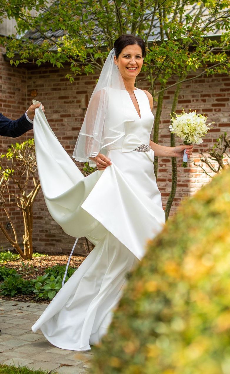 Bruid in een witte satijnen trouwjurk met boeket, sluier en sleep buiten.