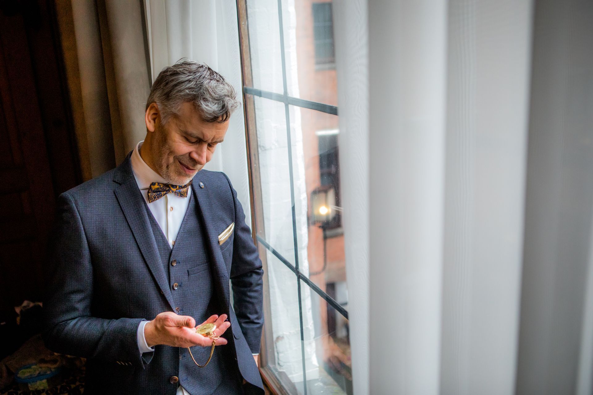 Een man in pak kijkt naar het voorwerp in zijn hand dat bij een raam staat.