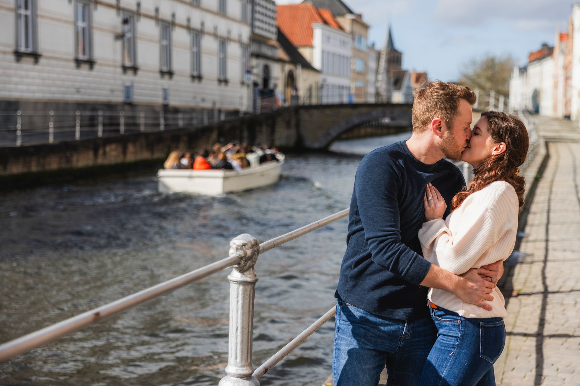Een kussend stelletje aan een kanaal met een boot, oude gebouwen op de achtergrond. Zonnige dag.