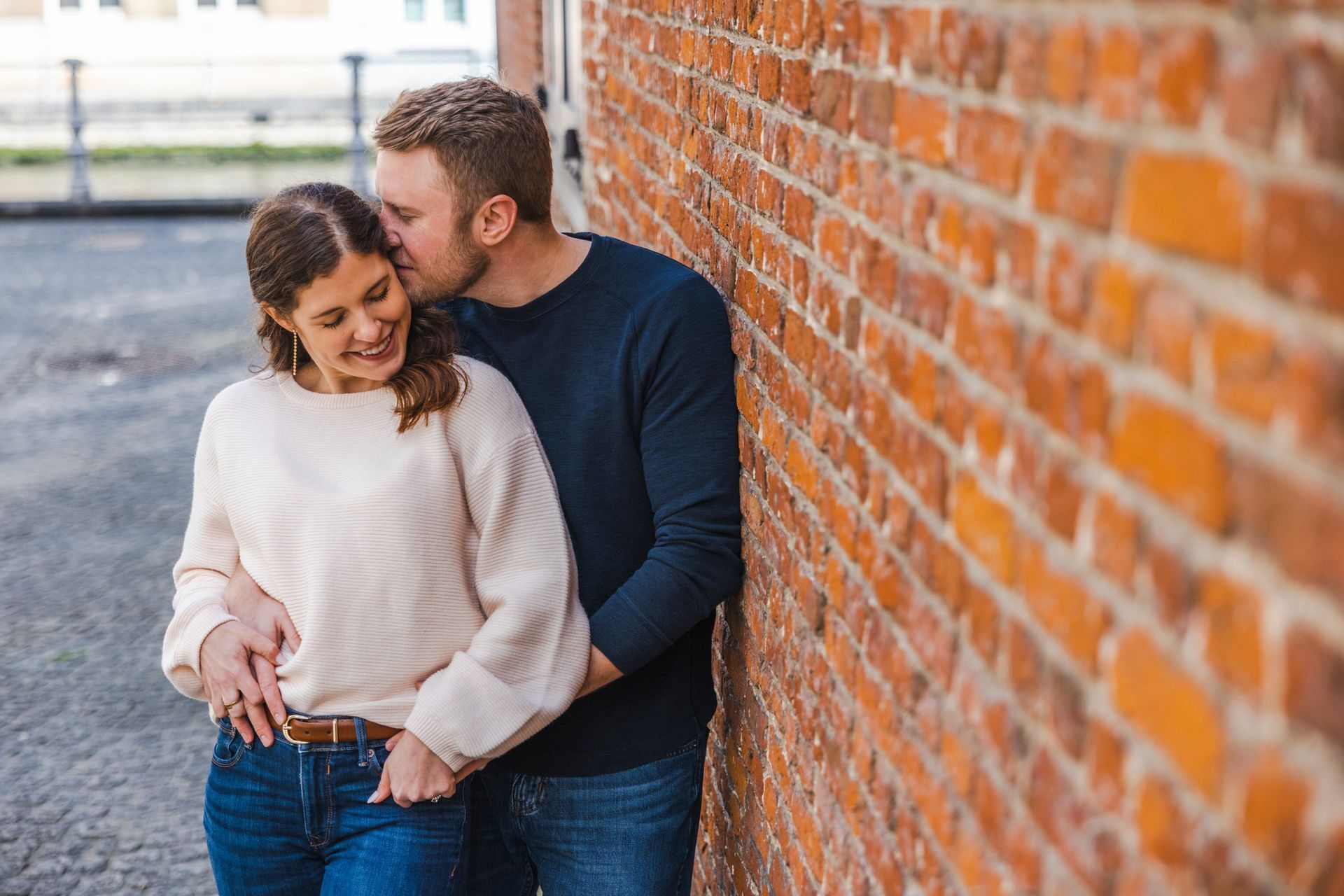 Man kust vrouw op voorhoofd naast een bakstenen muur. Ze lachen.