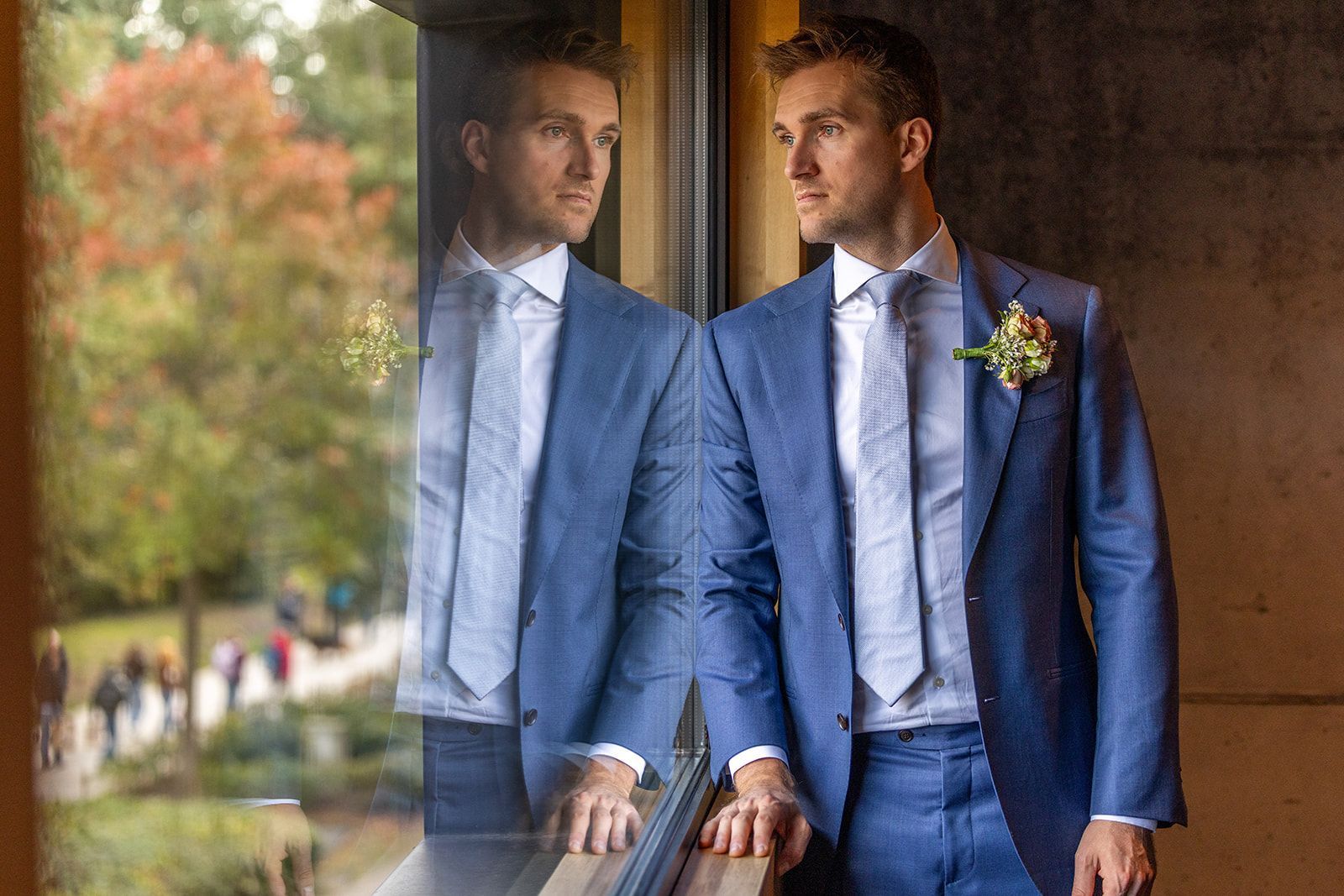 Een man in een blauw pak kijkt uit het raam en de weerspiegeling ervan in het glas.