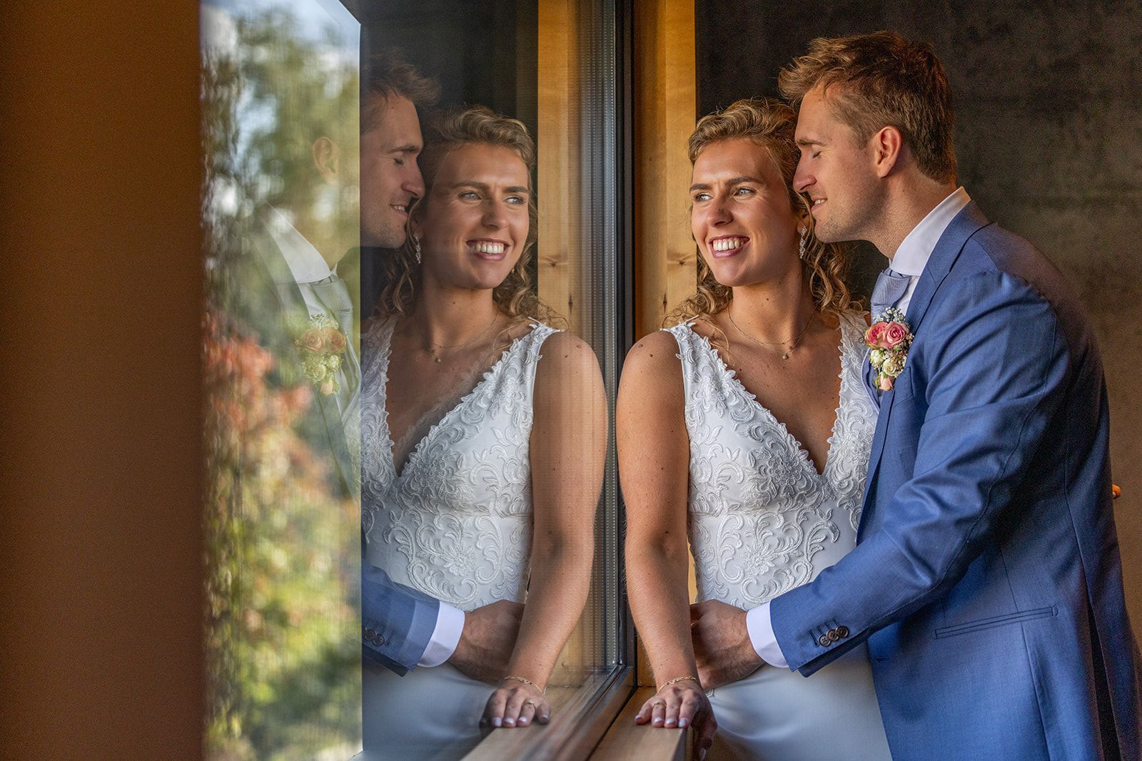 Het bruidspaar kijkt uit het raam, de bruidegom kust de wang van de bruid, weerspiegeld in het glas.