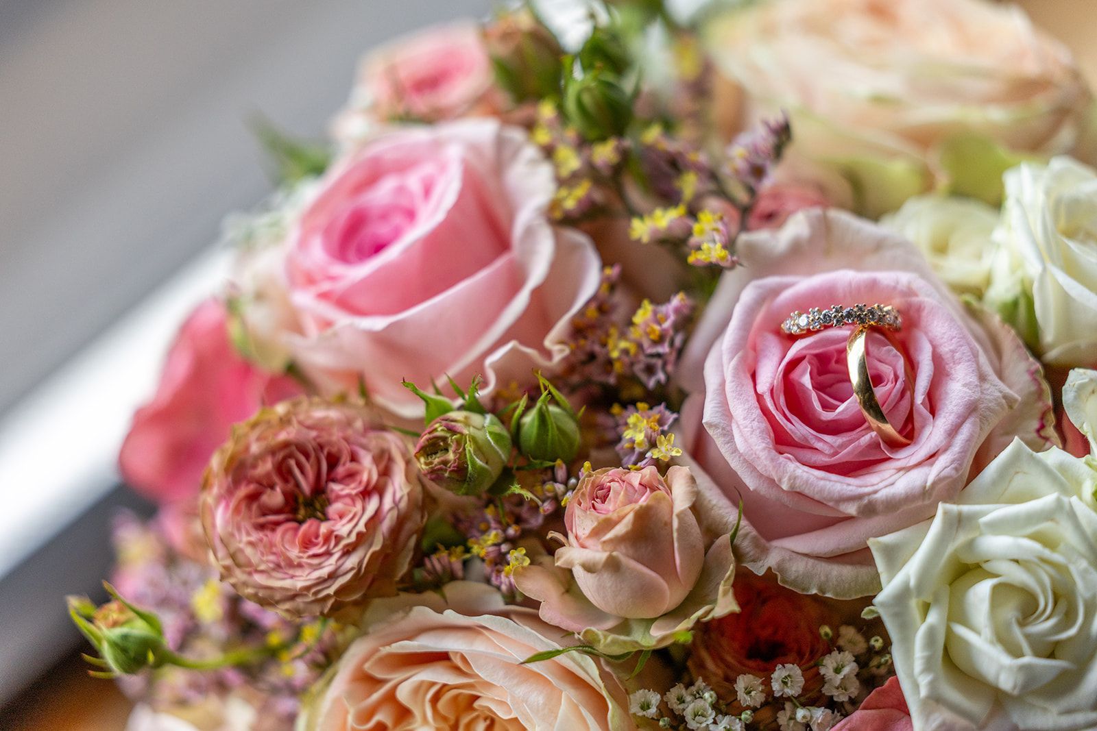 Trouwringen in een boeket van roze en perzikkleurige rozen.