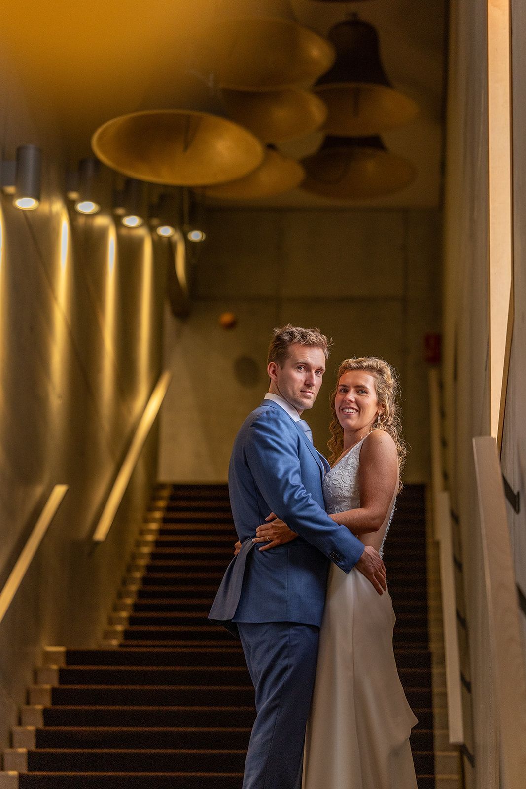 Een bruidspaar omhelst elkaar op een trap, warm licht verlicht de omgeving.