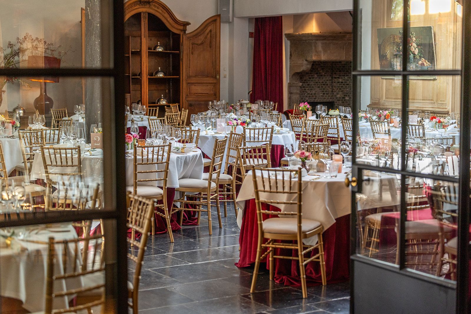 Interieur van een feestzaal, tafels gedekt met wit linnen, gouden stoelen en rode plinten.