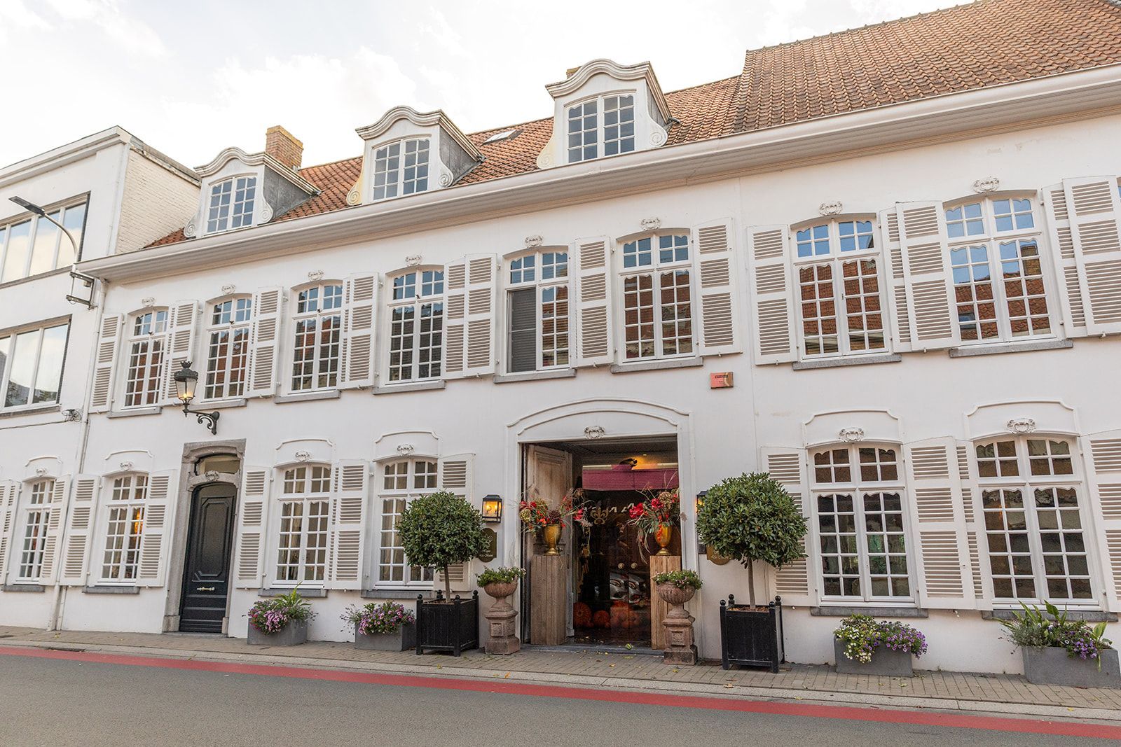 Wit gebouw met luiken en verschillende ramen; straatbeeld.