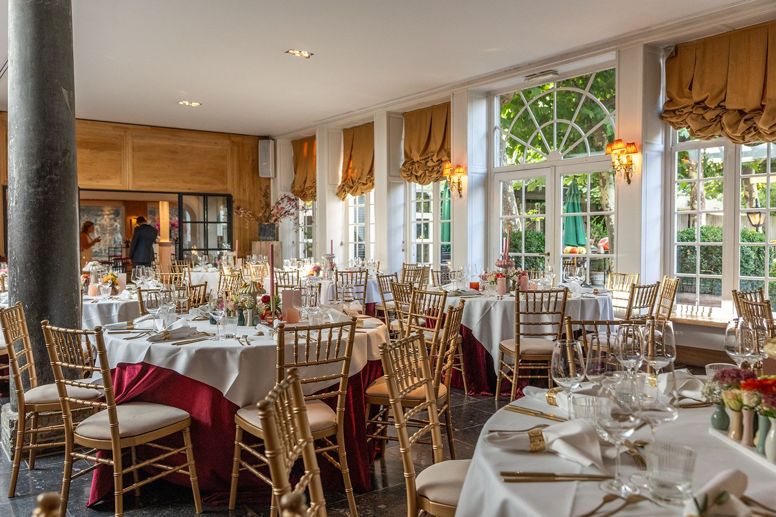 Formele eetkamer voor een feestje, met ronde tafels, gouden stoelen en grote ramen.